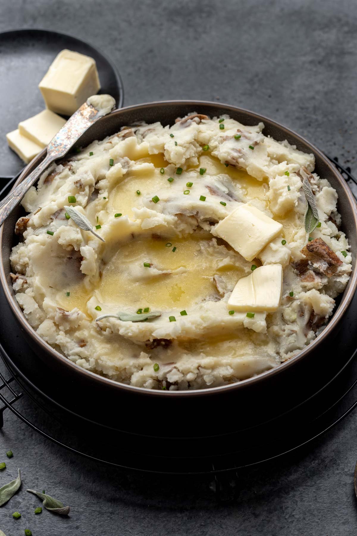 Mashed potatoes without milk in a serving bowl with butter and chives.