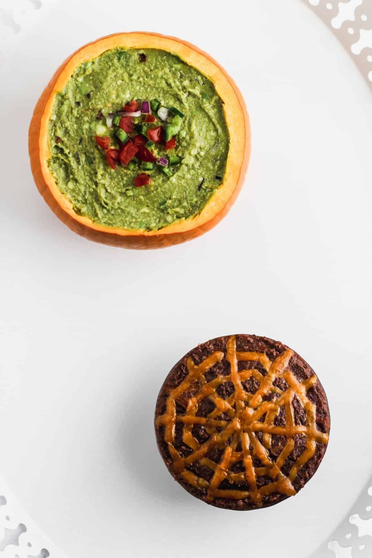 Guacamole and black bean dip in pumpkins on a white platter.