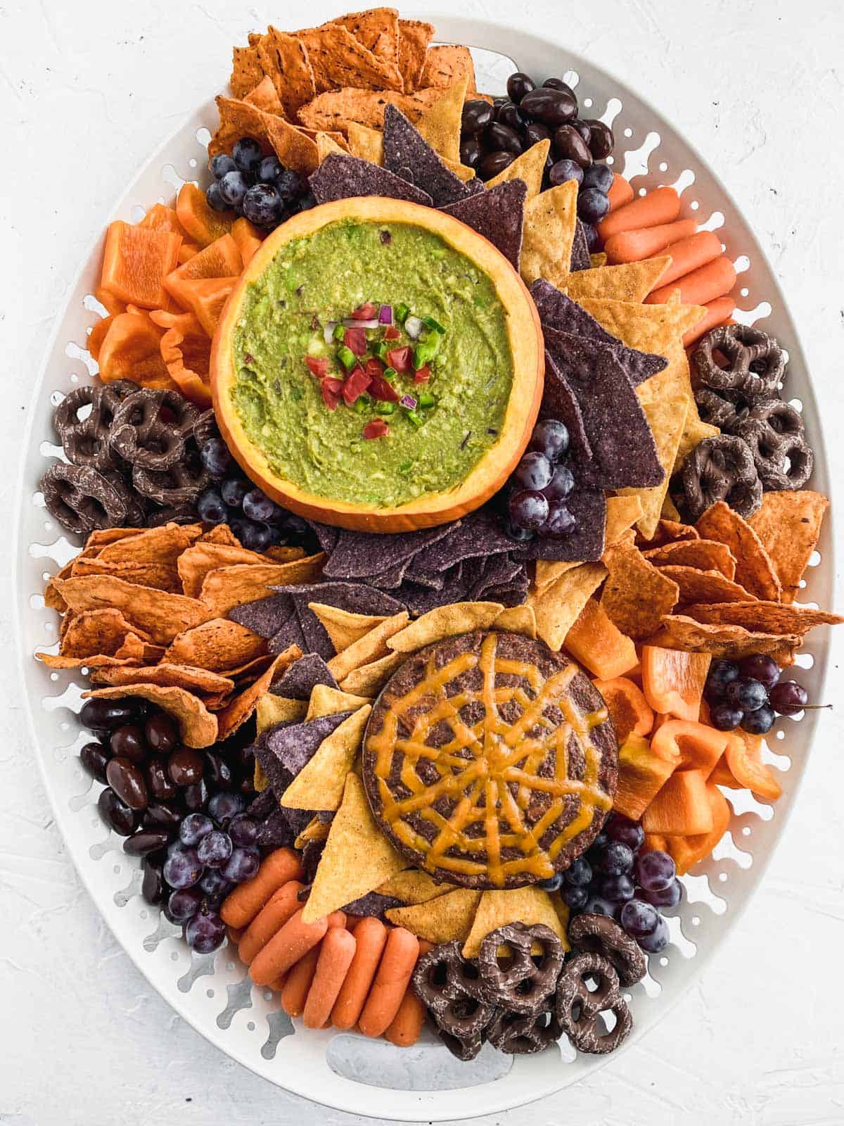 Halloween snack board on a large white platter with guacamole in a pumpkin and warm black bean dip.