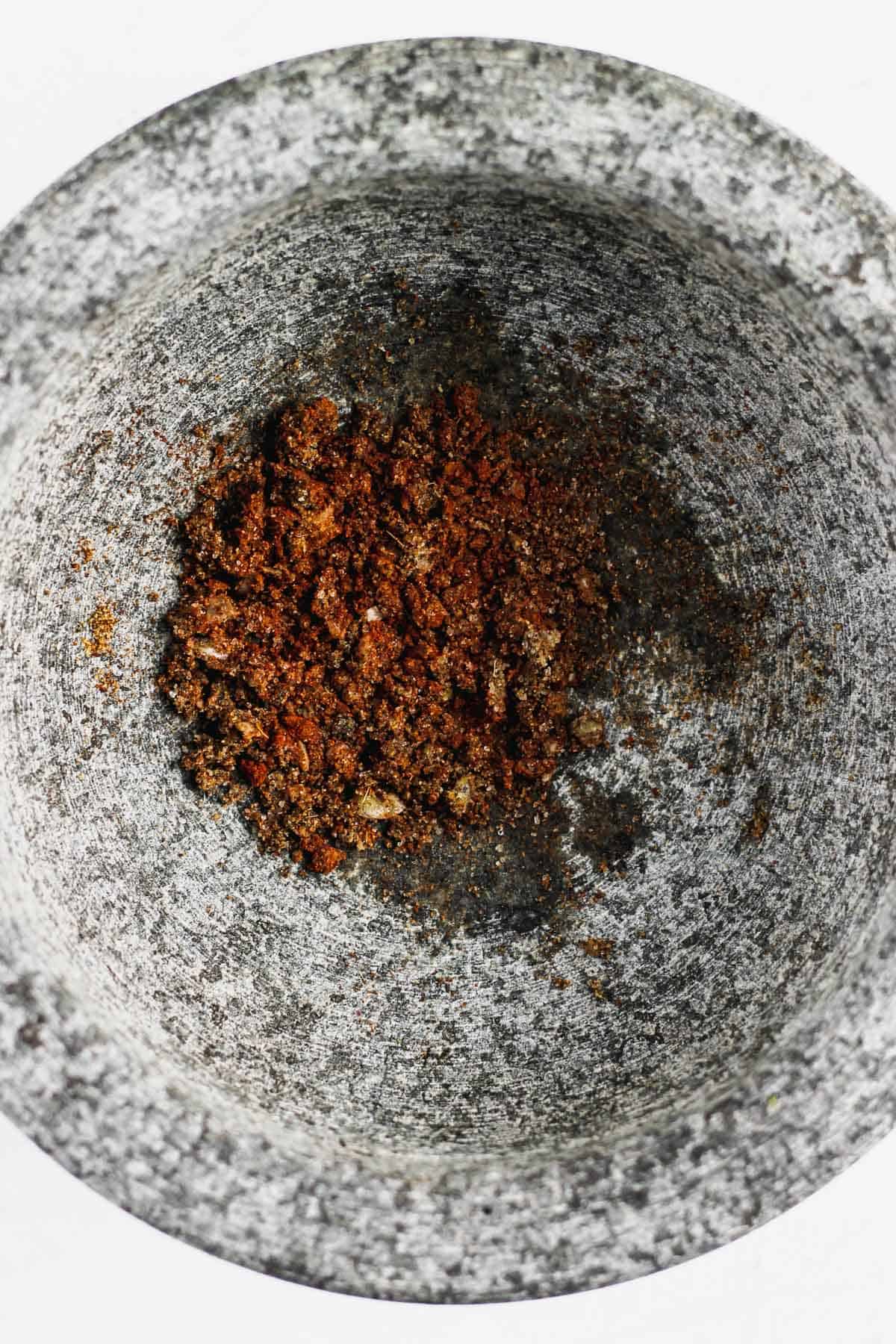 Minced garlic and spices in the form of a paste at the bottom of a gray stone mortar.