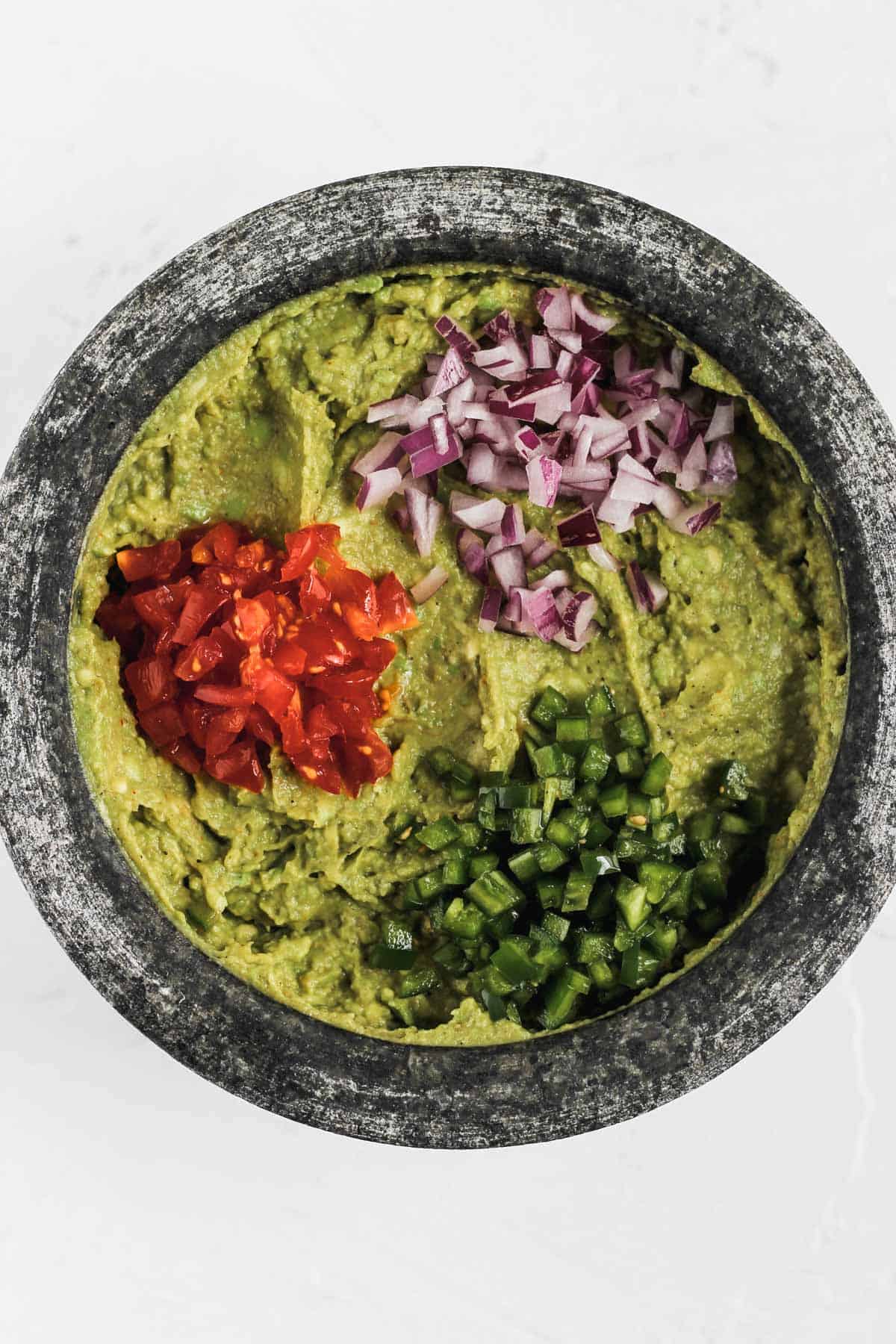 Tomatoes, red onions, and jalapeños on top of mashed avocados.