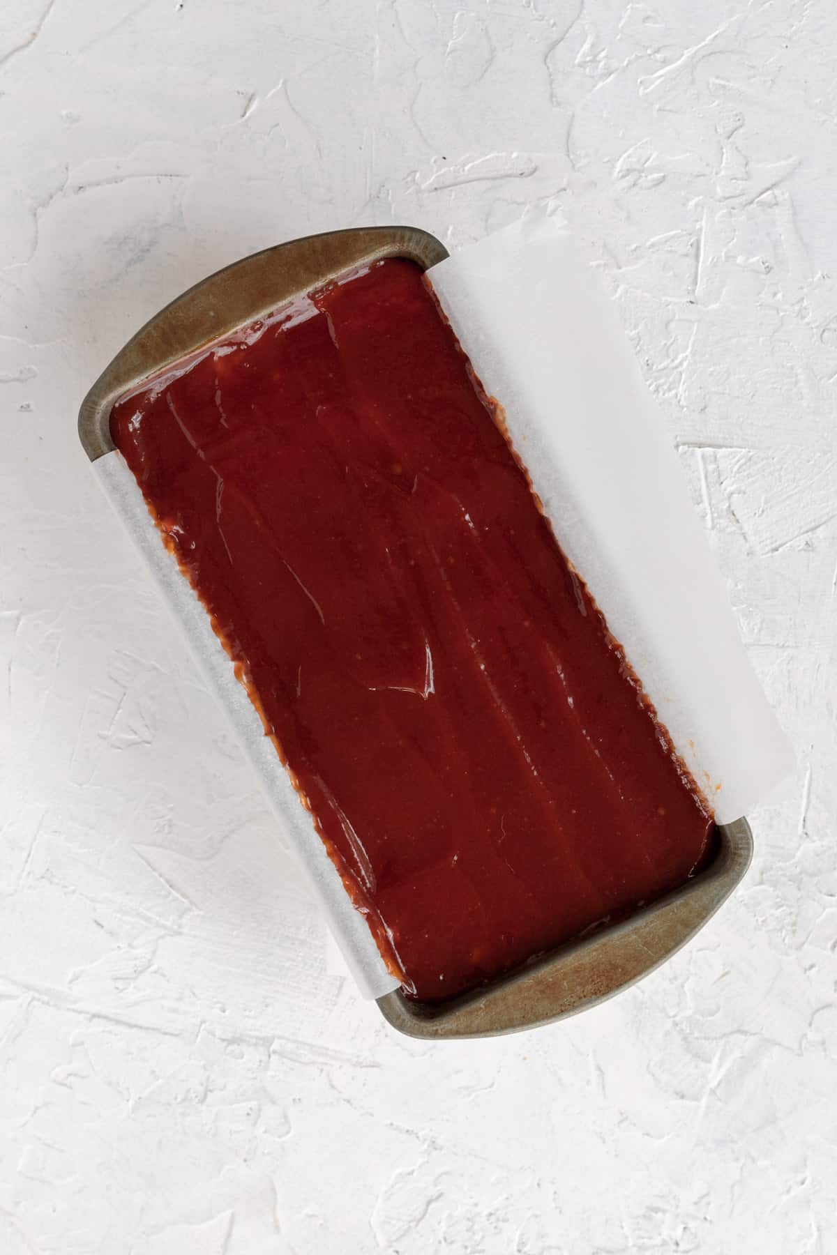 Uncooked meatloaf in a loaf pan topped with a ketchup glaze before going in the oven.