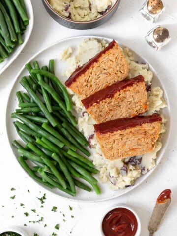 A dinner plate filled with mashed potatoes, green beans, and 3 slices of ground chicken meatloaf.