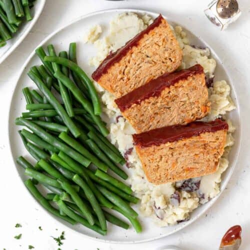 A dinner plate filled with mashed potatoes, green beans, and 3 slices of ground chicken meatloaf.