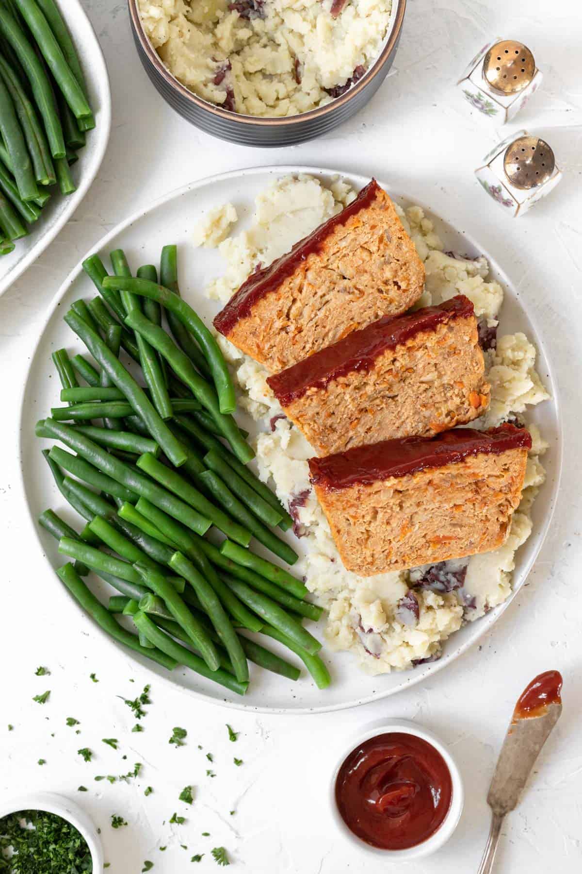 A dinner plate filled with mashed potatoes, green beans, and 3 slices of ground chicken meatloaf.