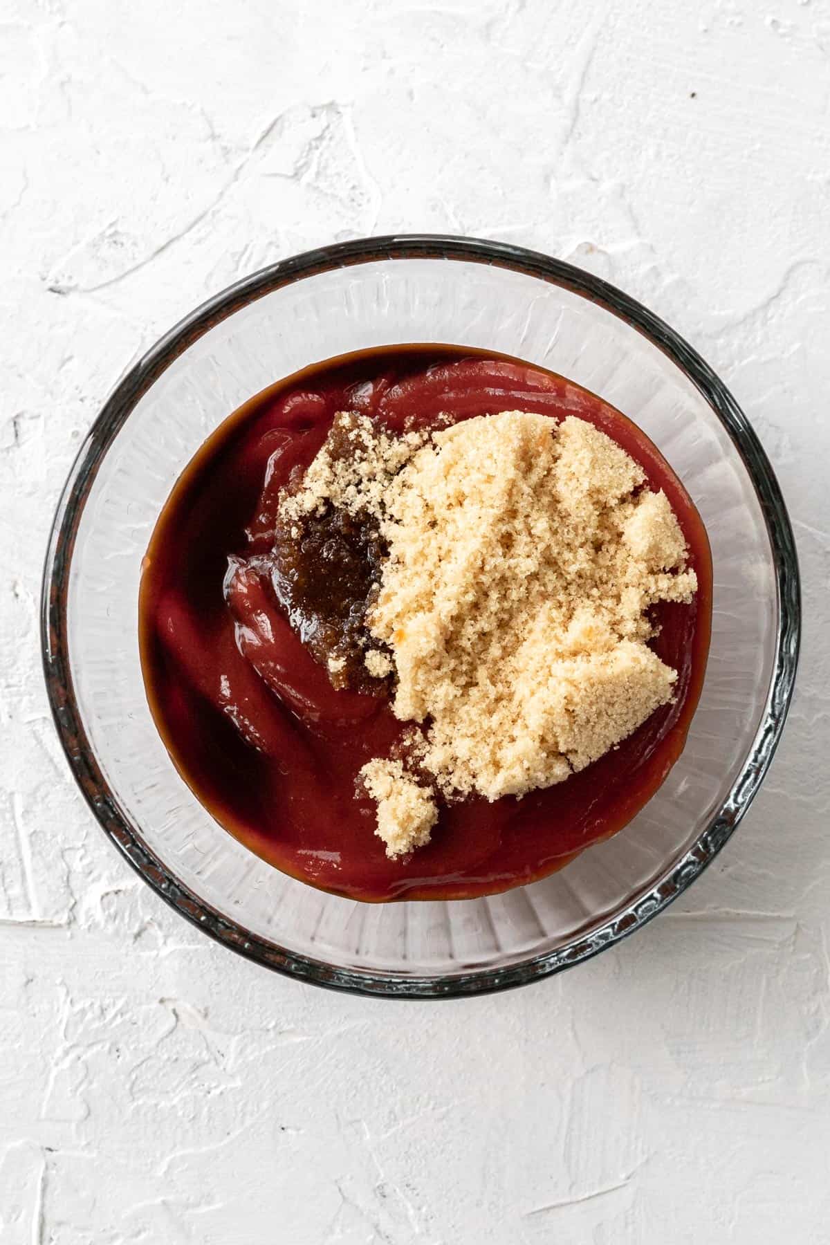 Ketchup topped with brown sugar and Worcestershire sauce in a glass bowl.