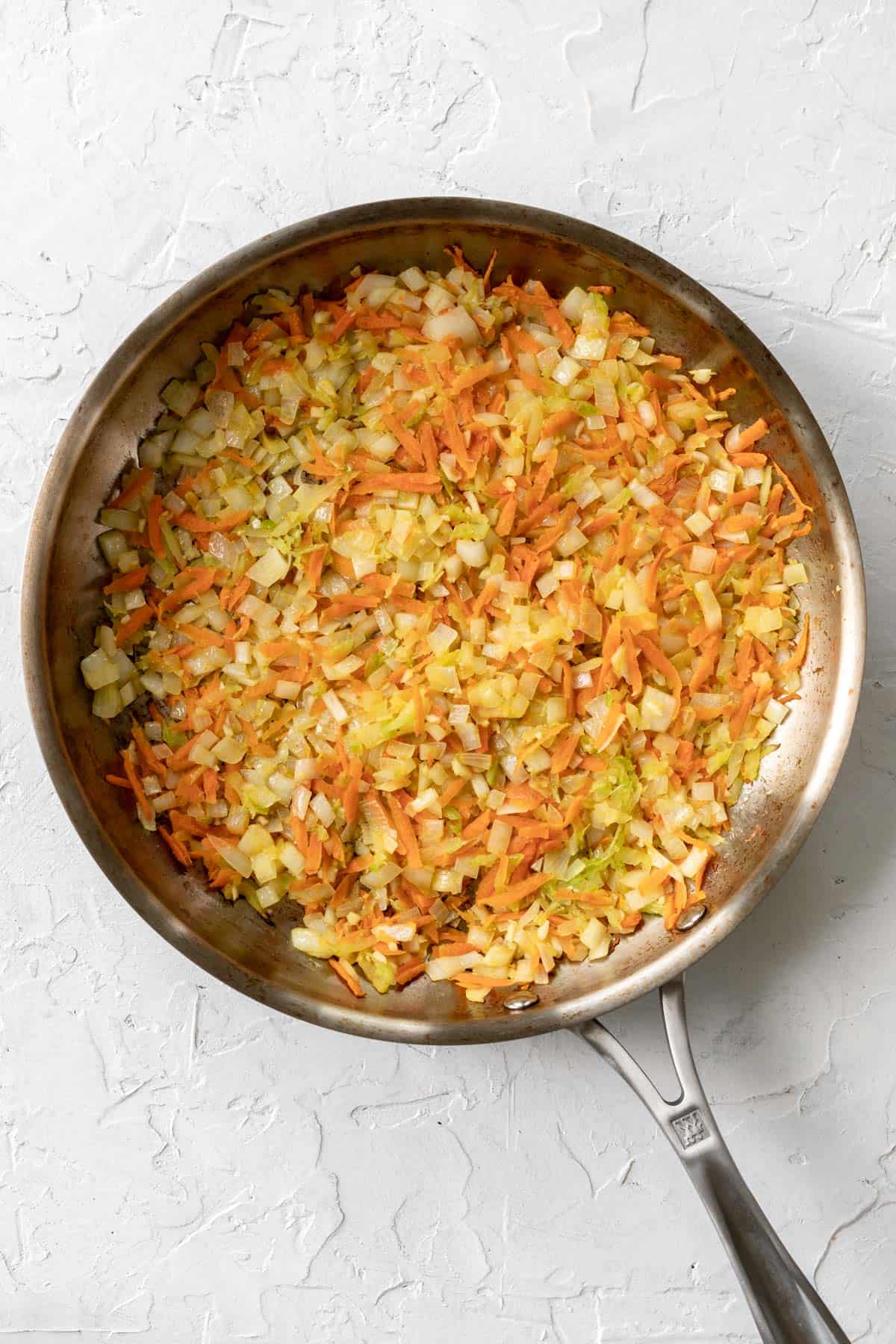 Shredded carrots, celery, onions, and garlic cooking in a metal skillet.
