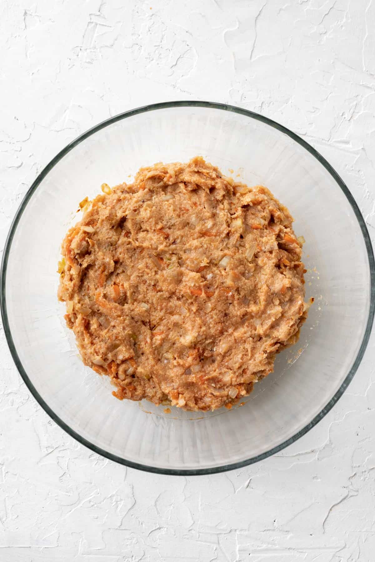 Ground chicken mixed with eggs, breadcrumbs, milk, ketchup, and vegetables in a glass bowl.