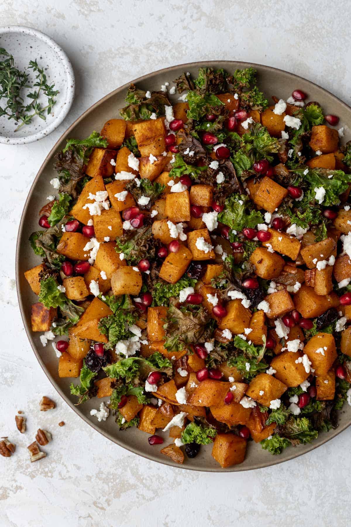 Roasted butternut squash with baked apples and crispy kale in a serving bowl with pomegranate seeds and feta on top.