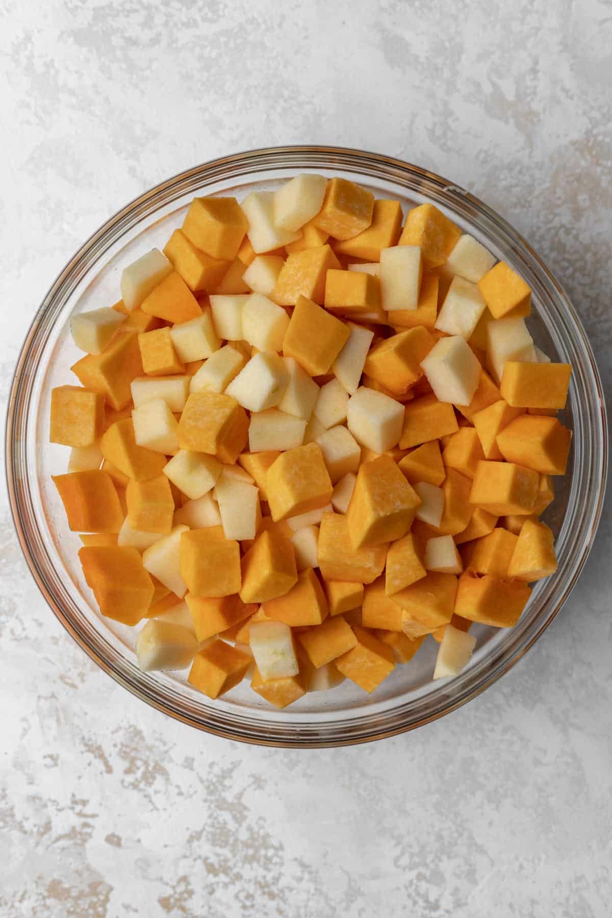 Diced and peeled butternut squash and apples in a glass mixing bowl.