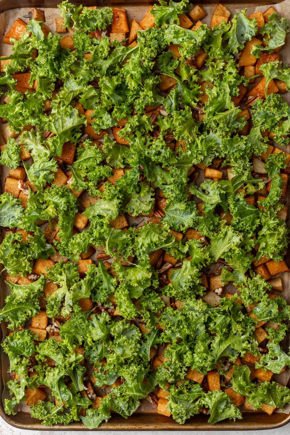 Chopped kale on top of butternut squash and apples on a sheet pan.