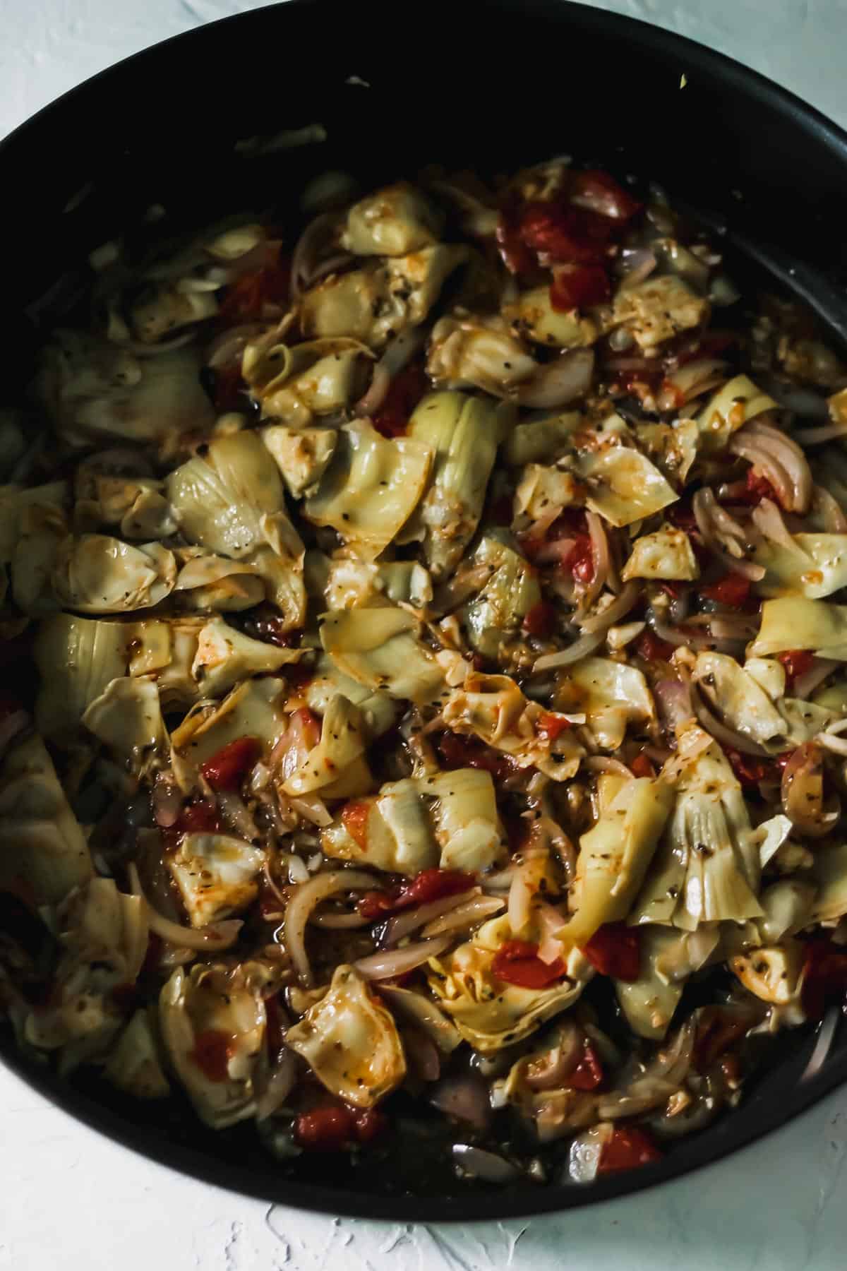 Olive oil, artichokes, garlic, shallots, and tomato in a high sided skillet.