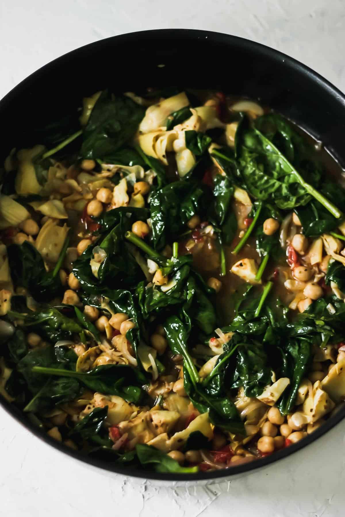 Olive oil, garlic, shallots, tomatoes, garbanzo beans, and spinach in a high sided skillet.