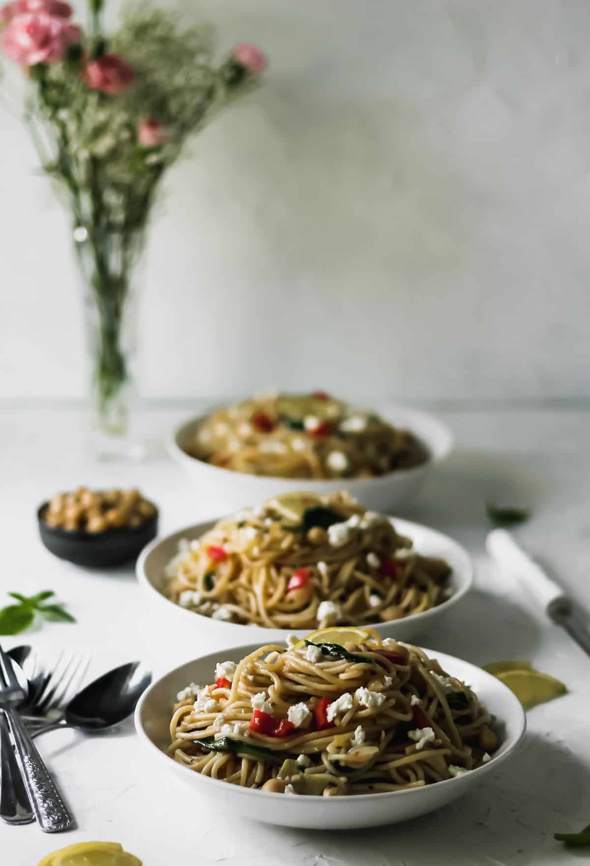 3 bowls of pasta with a vase of flowers behind them.