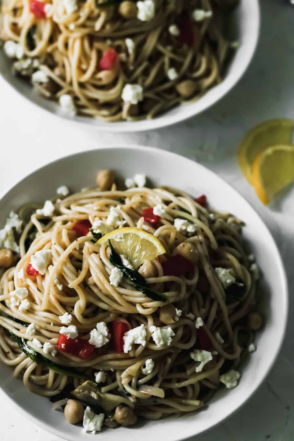 Mediterranean garlic and olive oil pasta in a white bowl with lemons on the side.