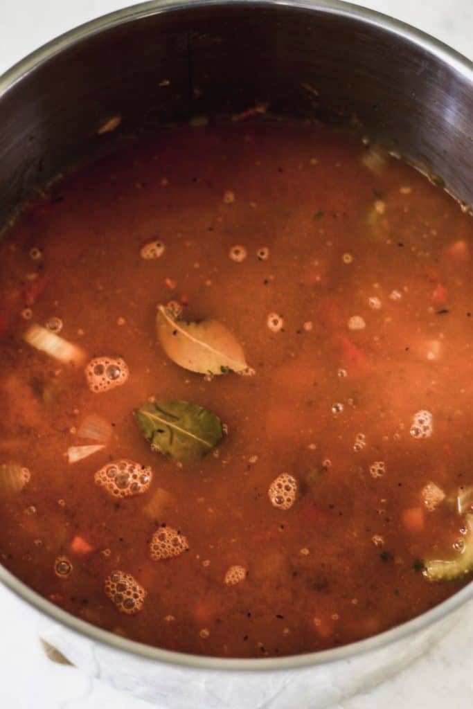 Vegetables, bay leaf, barley, and beans in a pot covered in vegetable broth.