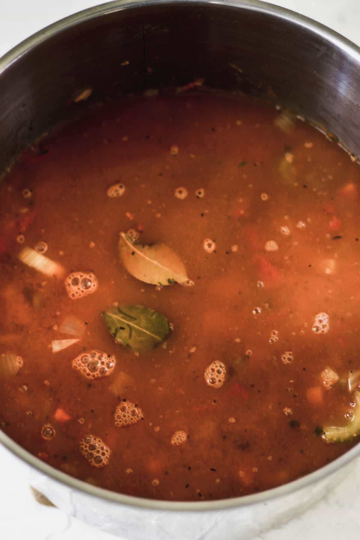 Vegetables, bay leaf, barley, and beans in a pot covered in vegetable broth.