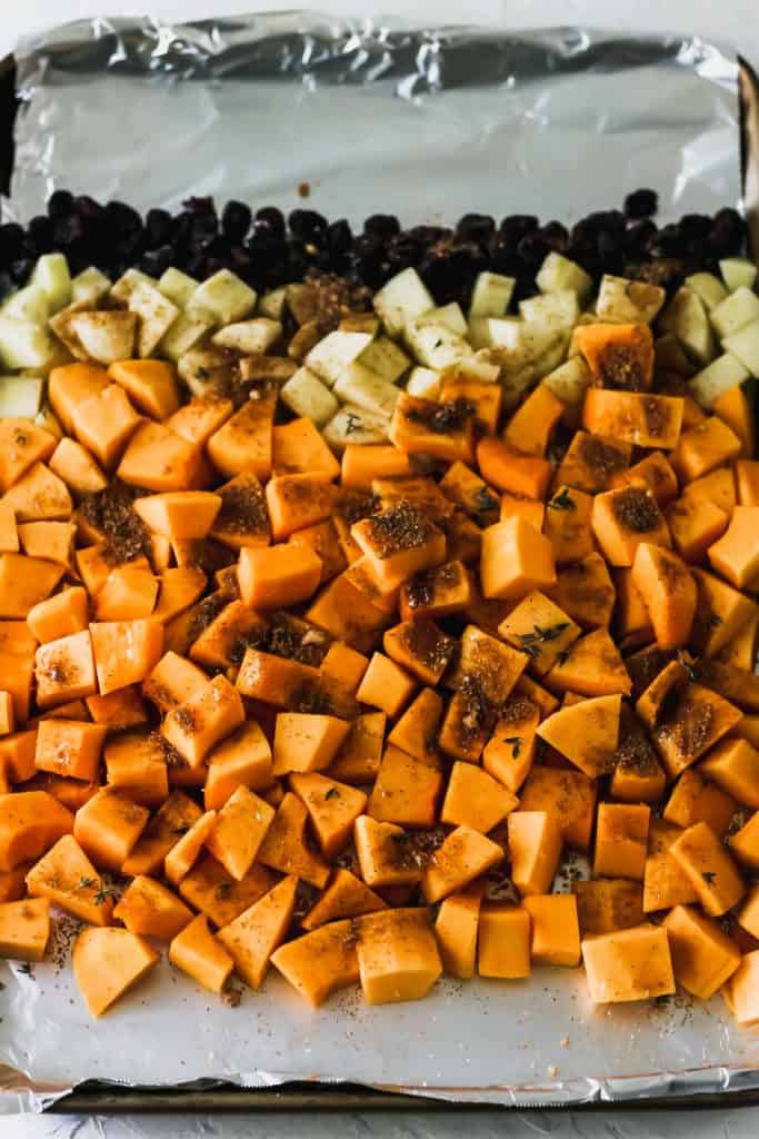 Squash, apples, and cranberries on a foil lined sheet pan with spices on top.
