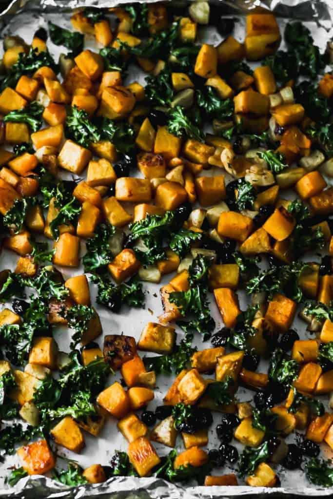 Roasted butternut squash, apples, cranberries, and kale on a foil lined sheet pan.