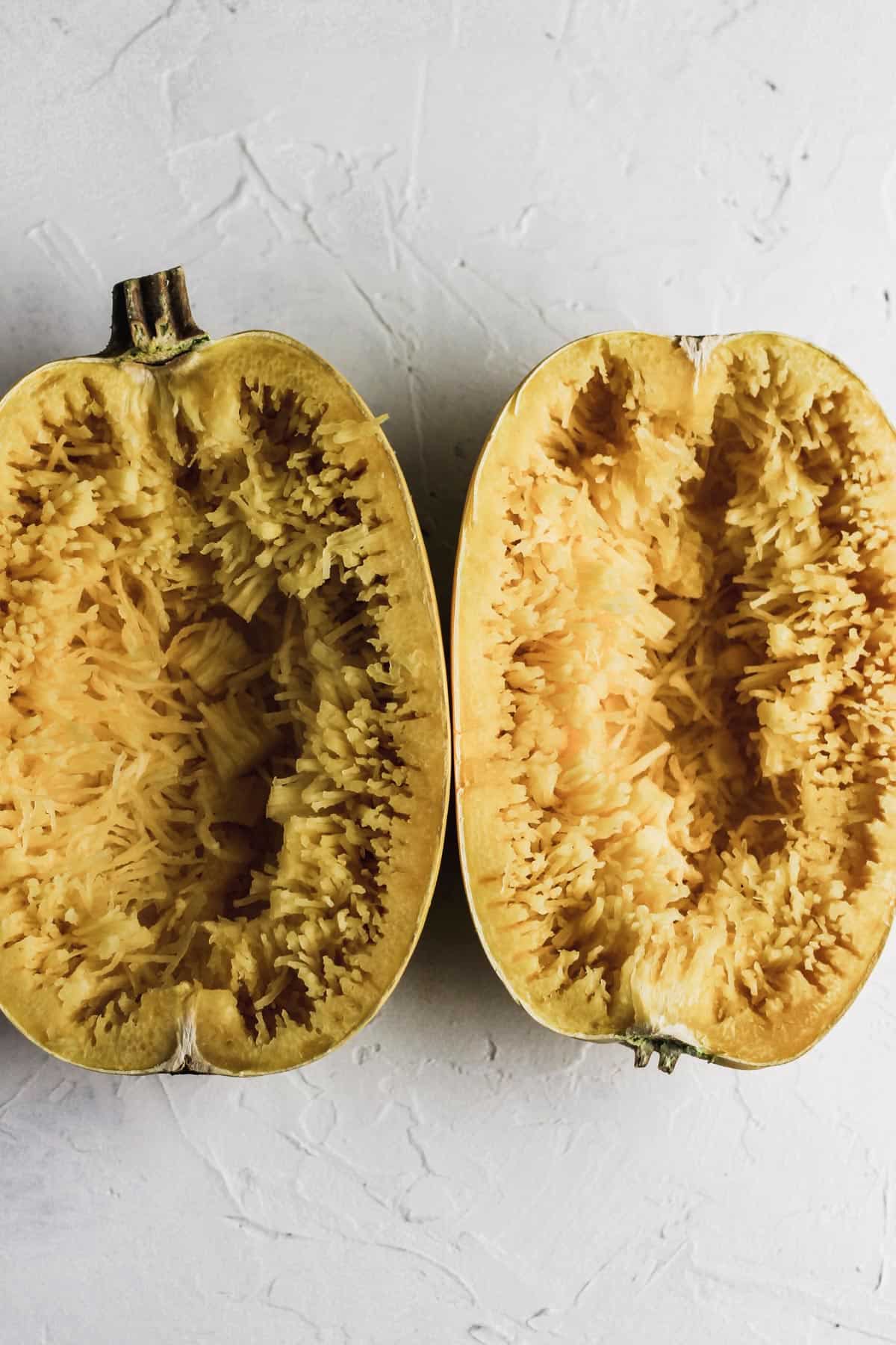 Halved cooked spaghetti squash with spaghetti strands pulled out with a fork.