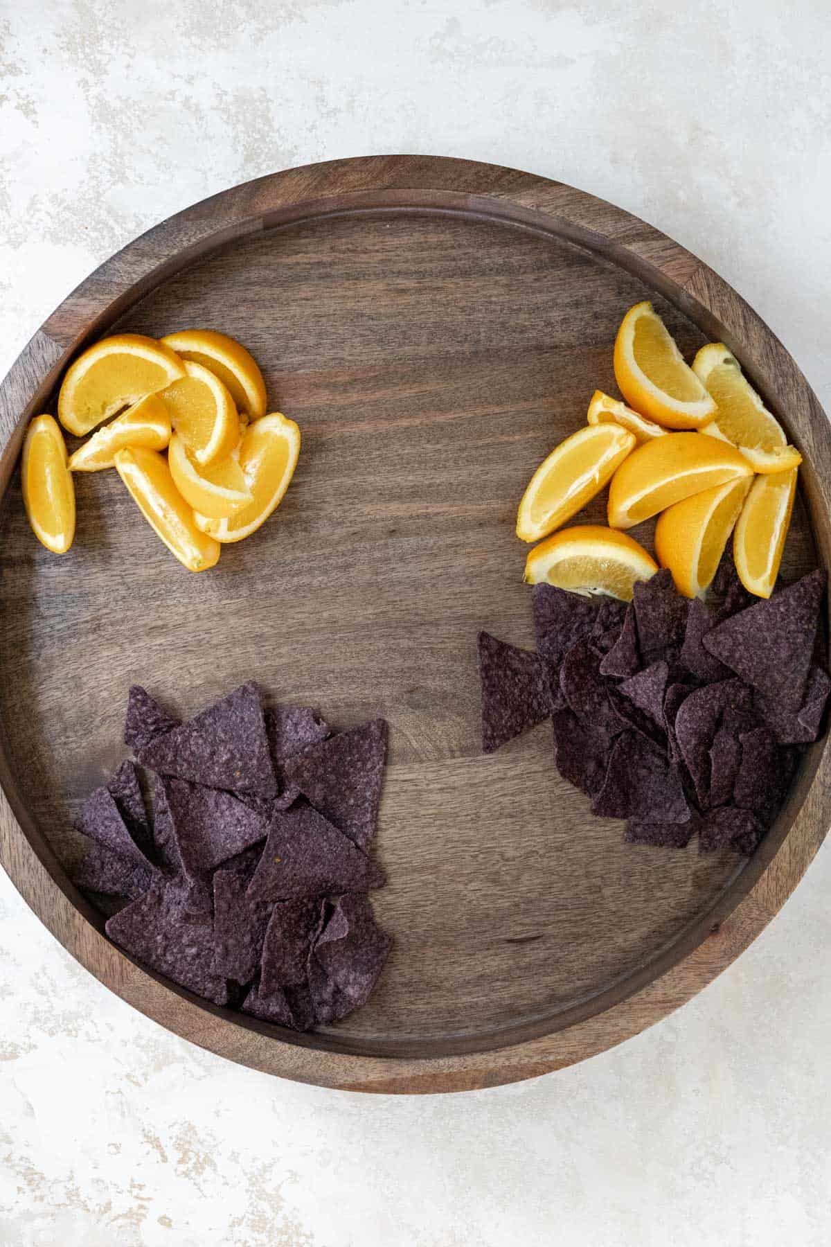 Orange wedges and blue corn tortilla chips arranged on a wooden board.