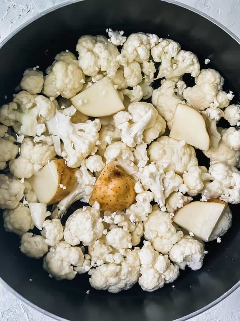 Cauliflower florets and cubed potato covered with water in a stock pot.