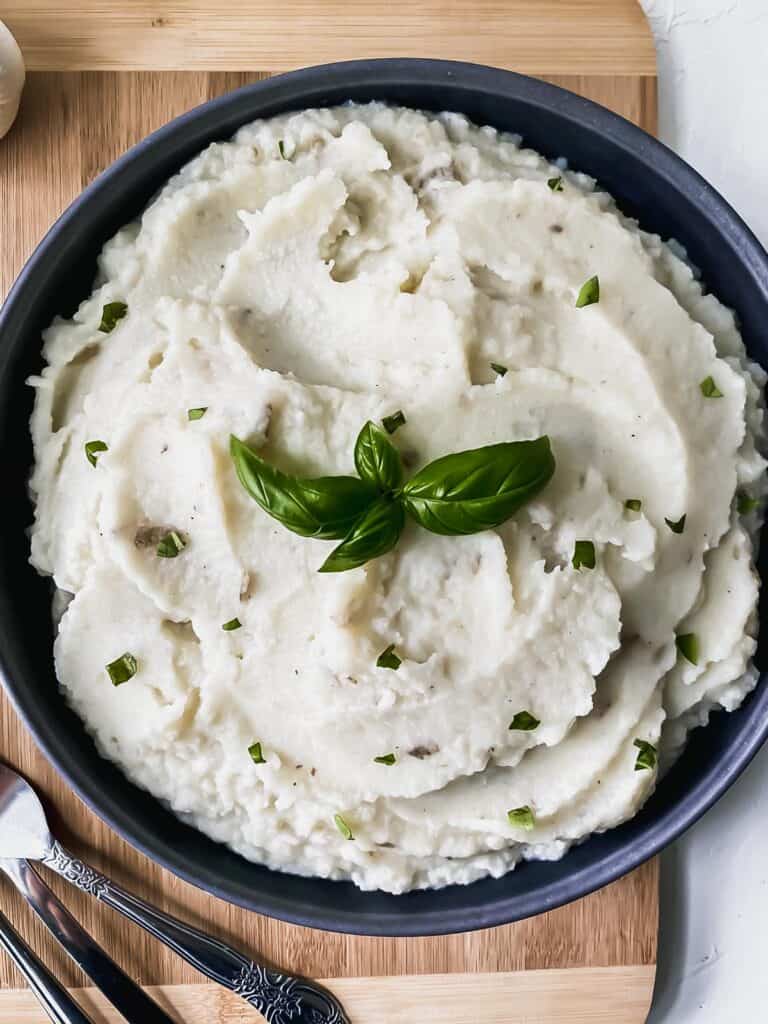Garlic cauliflower mashed potatoes in a black bowl with a garnish of basil.