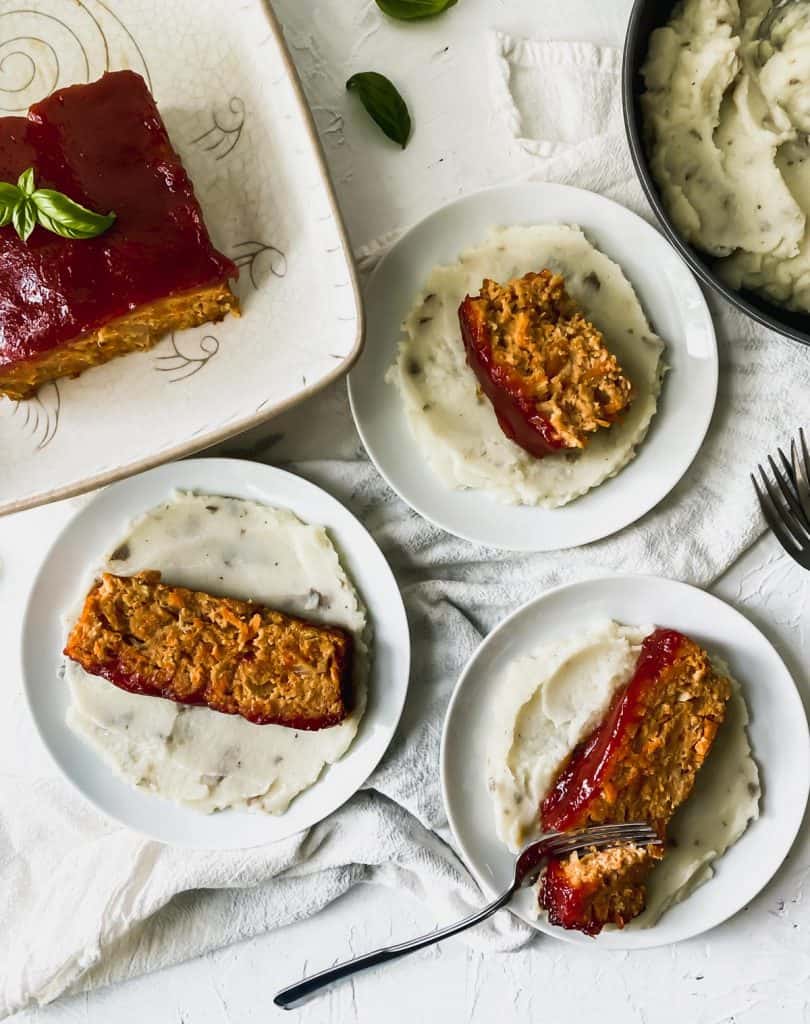 3 slices of healthy chicken meatloaf with hidden veggies on white plates with cauliflower mashed potatoes.