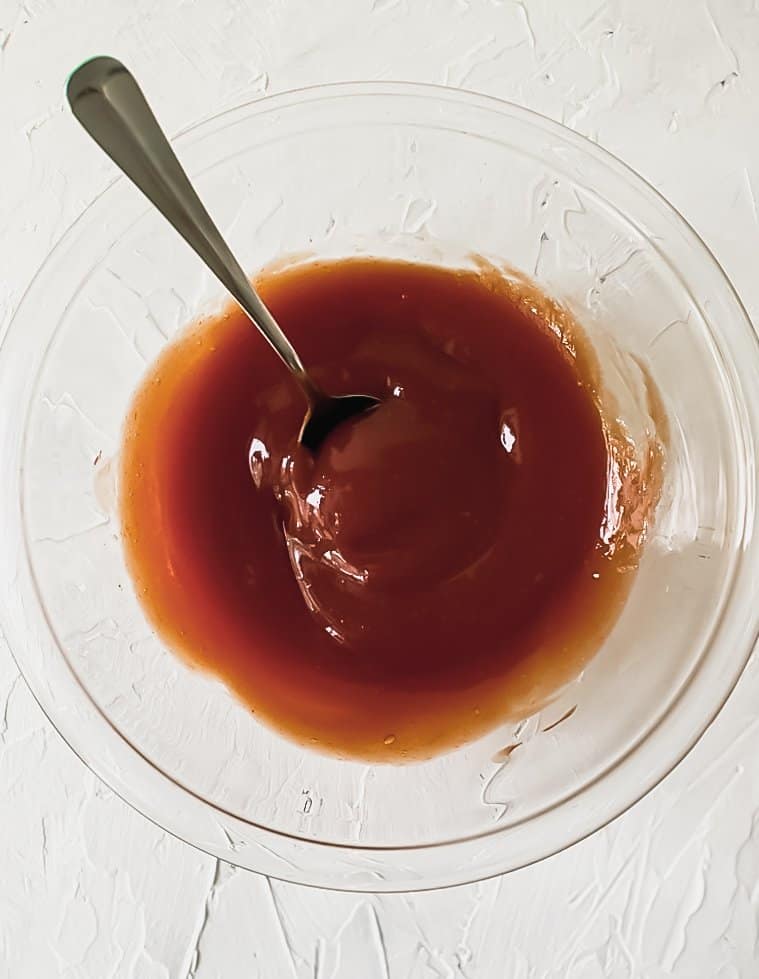 Combined ketchup, brown sugar, and worcestershire sauce in a glass bowl with a spoon.