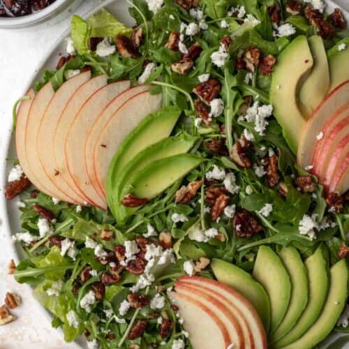 Arugula salad topped with sliced apples and avocado, maple toasted pecans, and feta with cranberry dressing on the side.