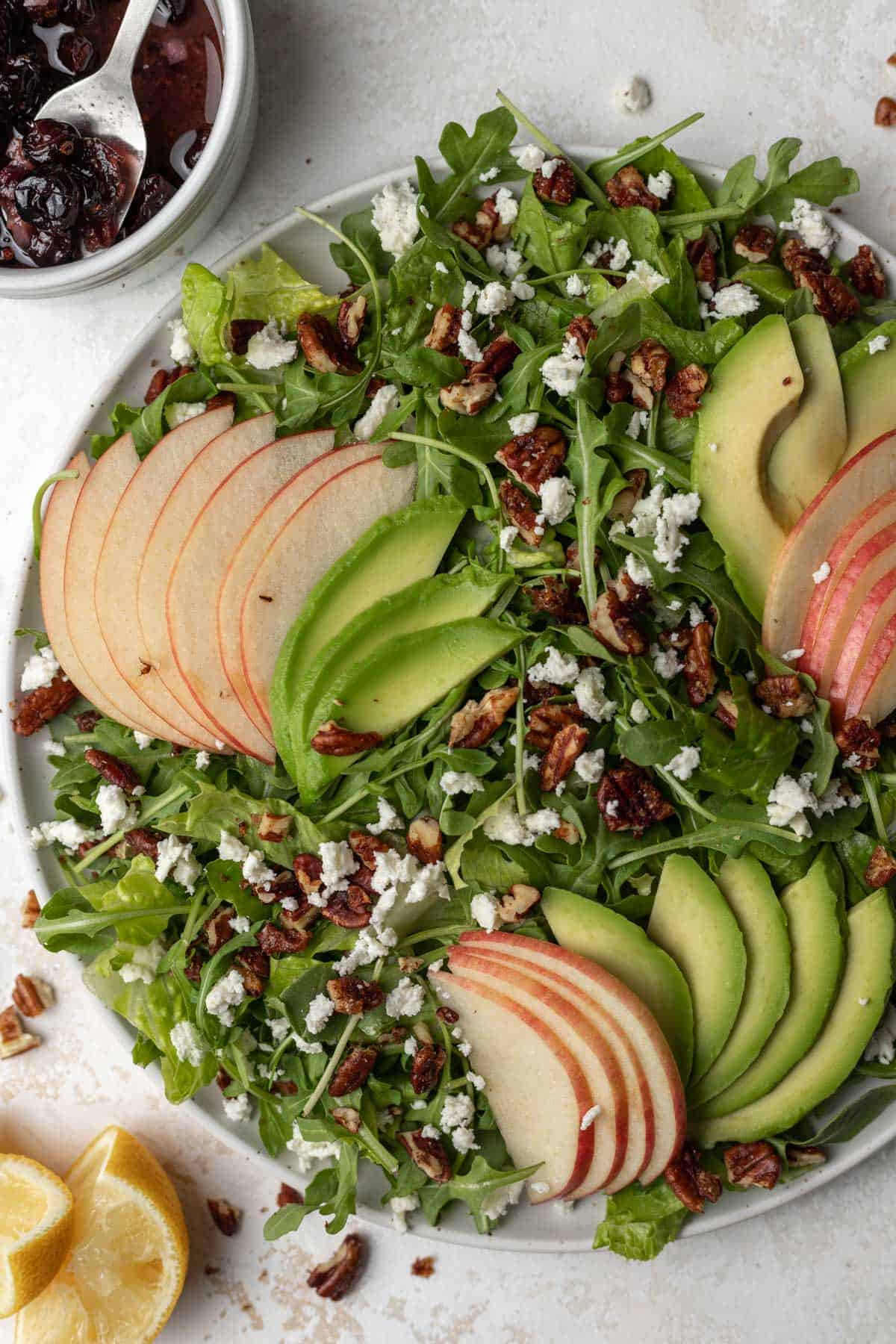 Arugula salad topped with sliced apples and avocado, maple toasted pecans, and feta with cranberry dressing on the side.