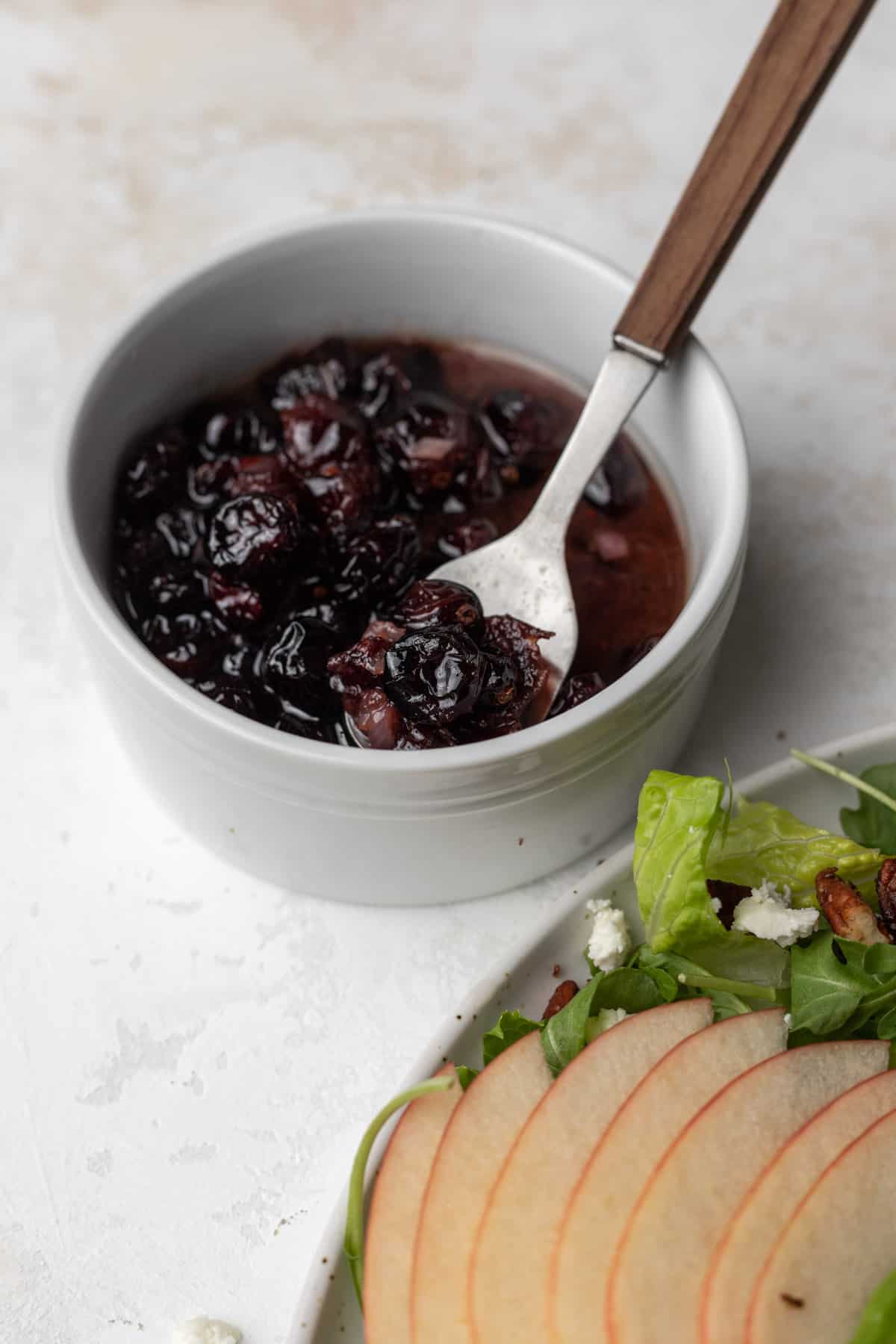 A closeup view of the homemade warm cranberry vinaigrette in a small bowl on the side of the arugula salad.