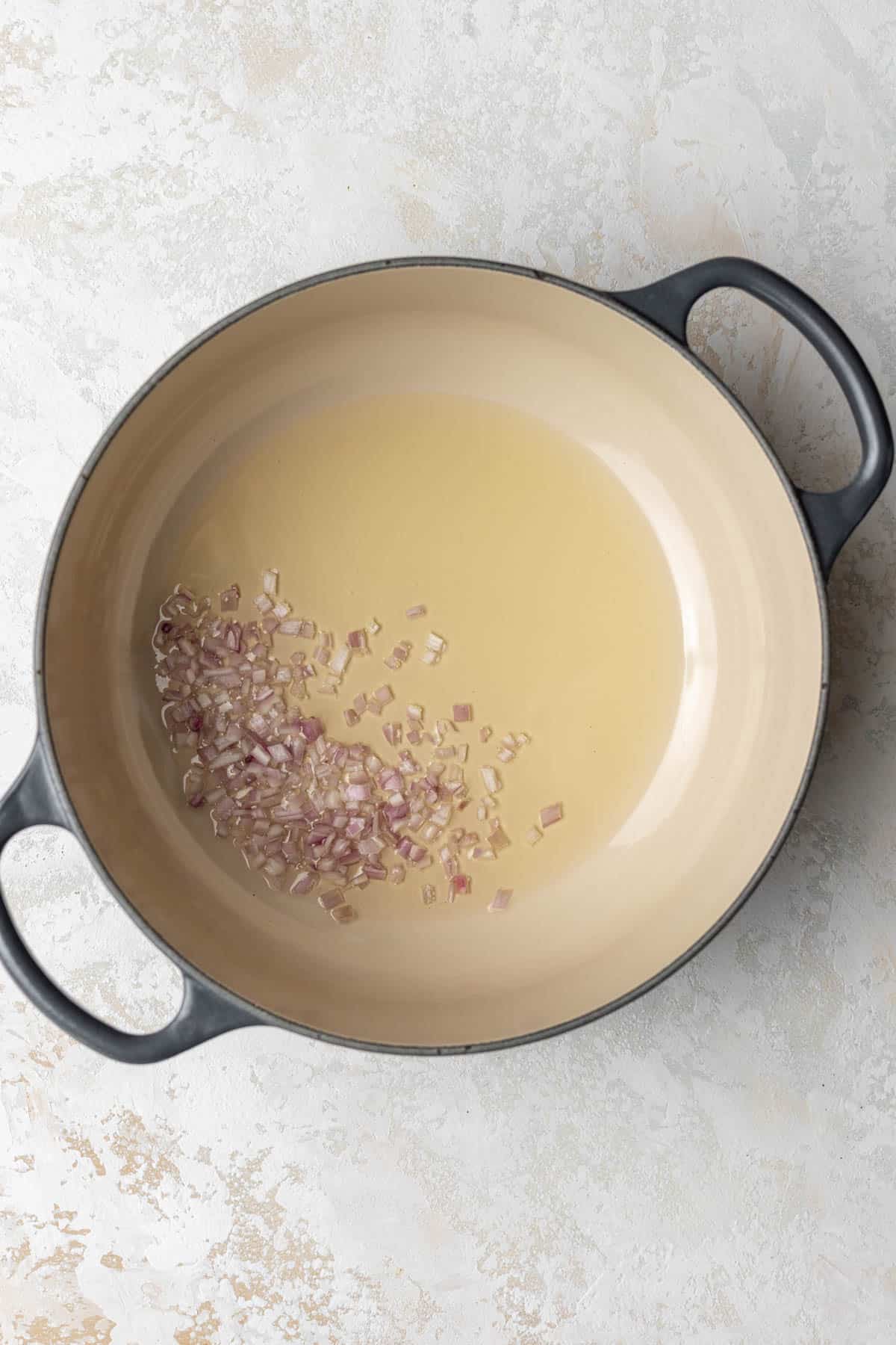 Finely diced shallots in a pot with olive oil.
