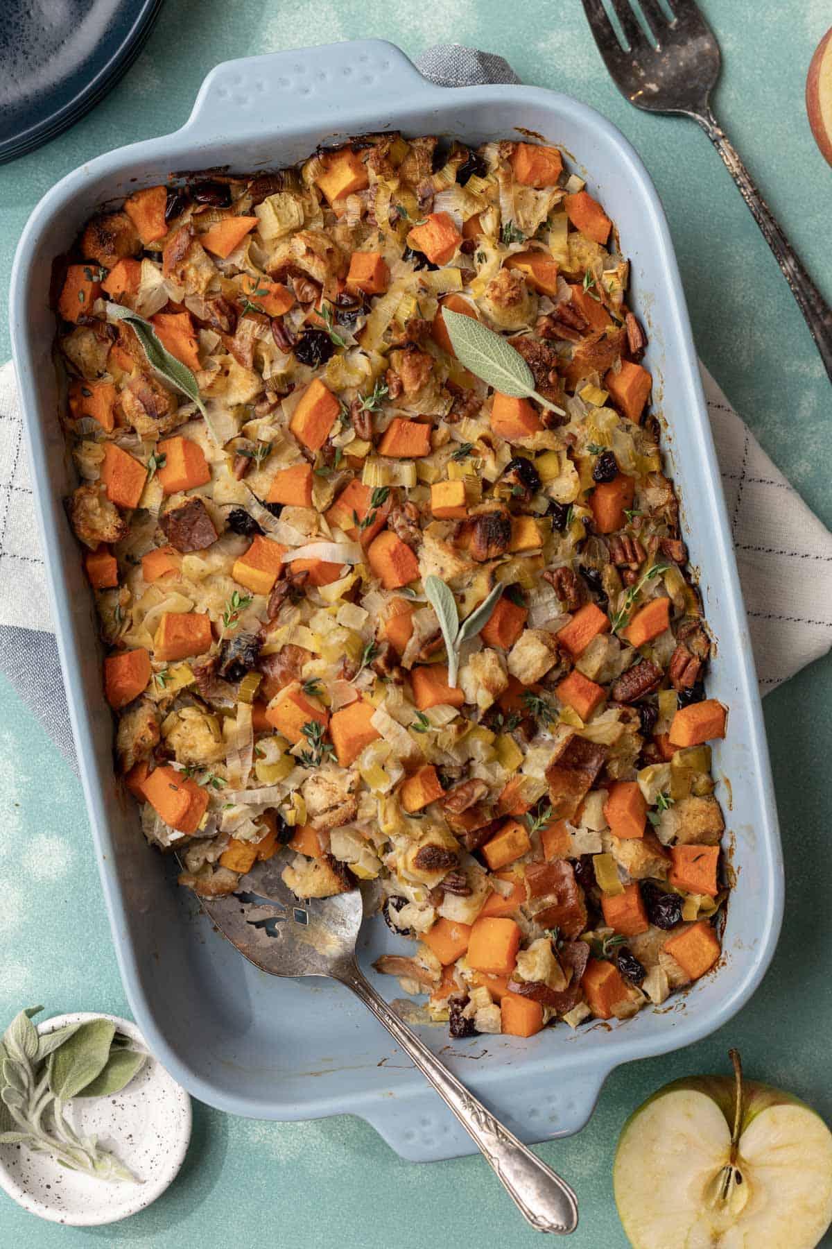 Baked butternut squash and apple stuffing in a blue baking dish with a serving spatula.
