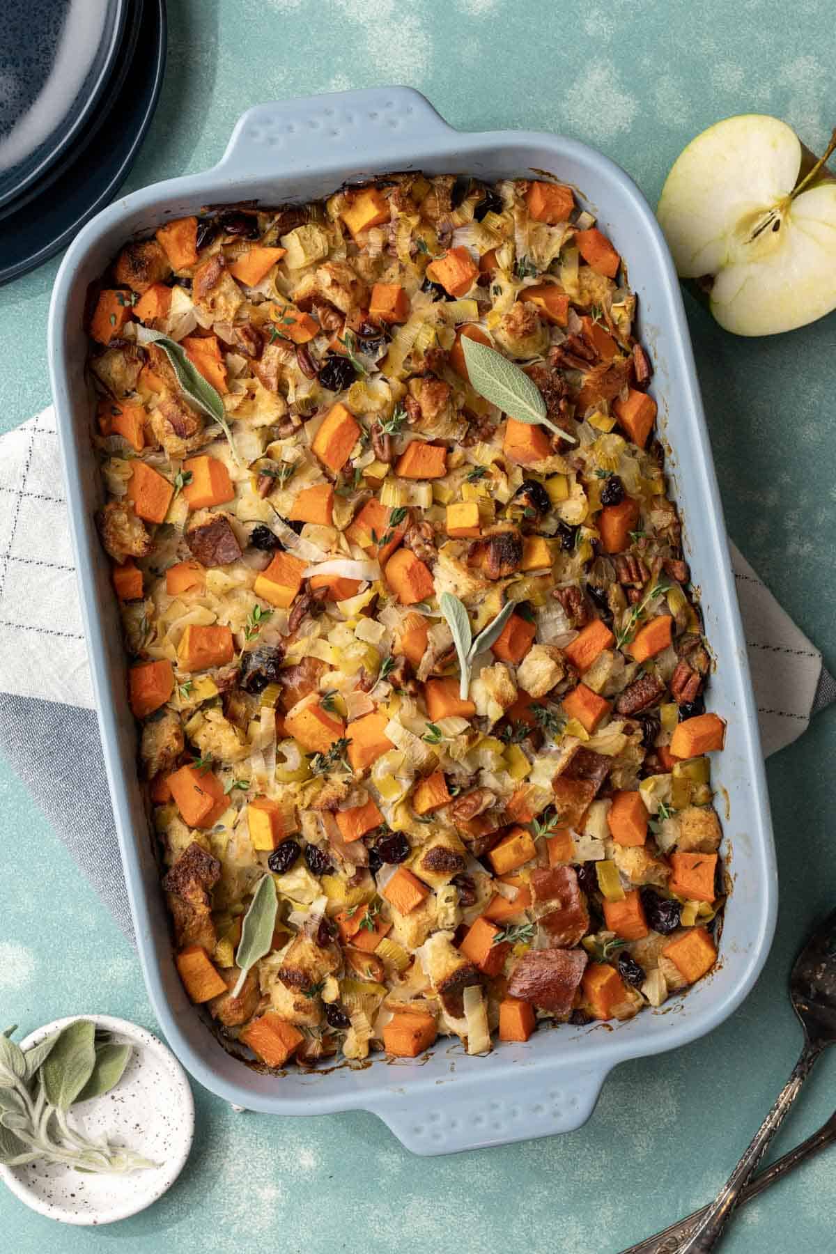 Baked butternut squash stuffing in a baking dish with sage and apples around it.