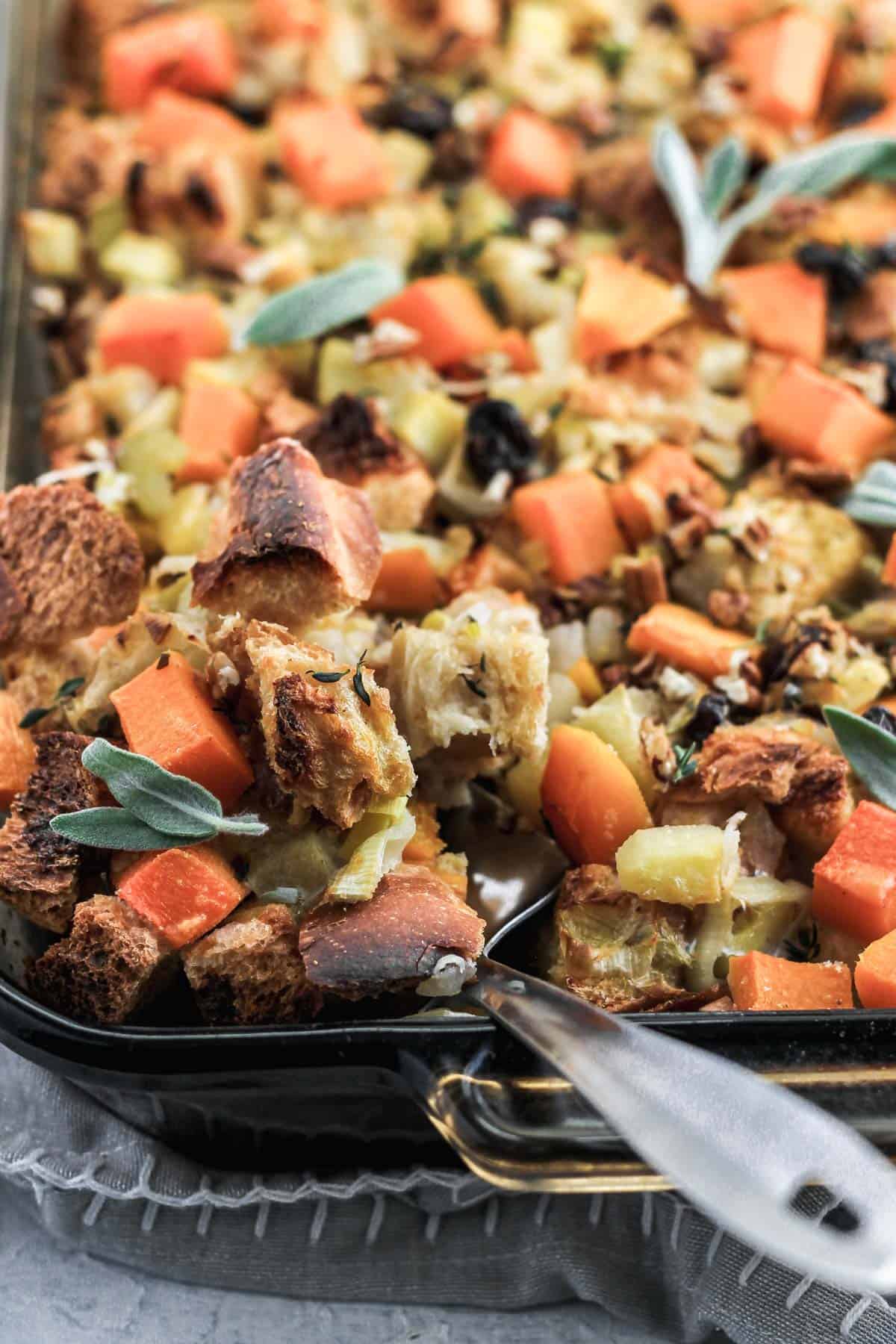 Butternut squash stuffing in a glass dish with a metal spatula scooping out some stuffing.