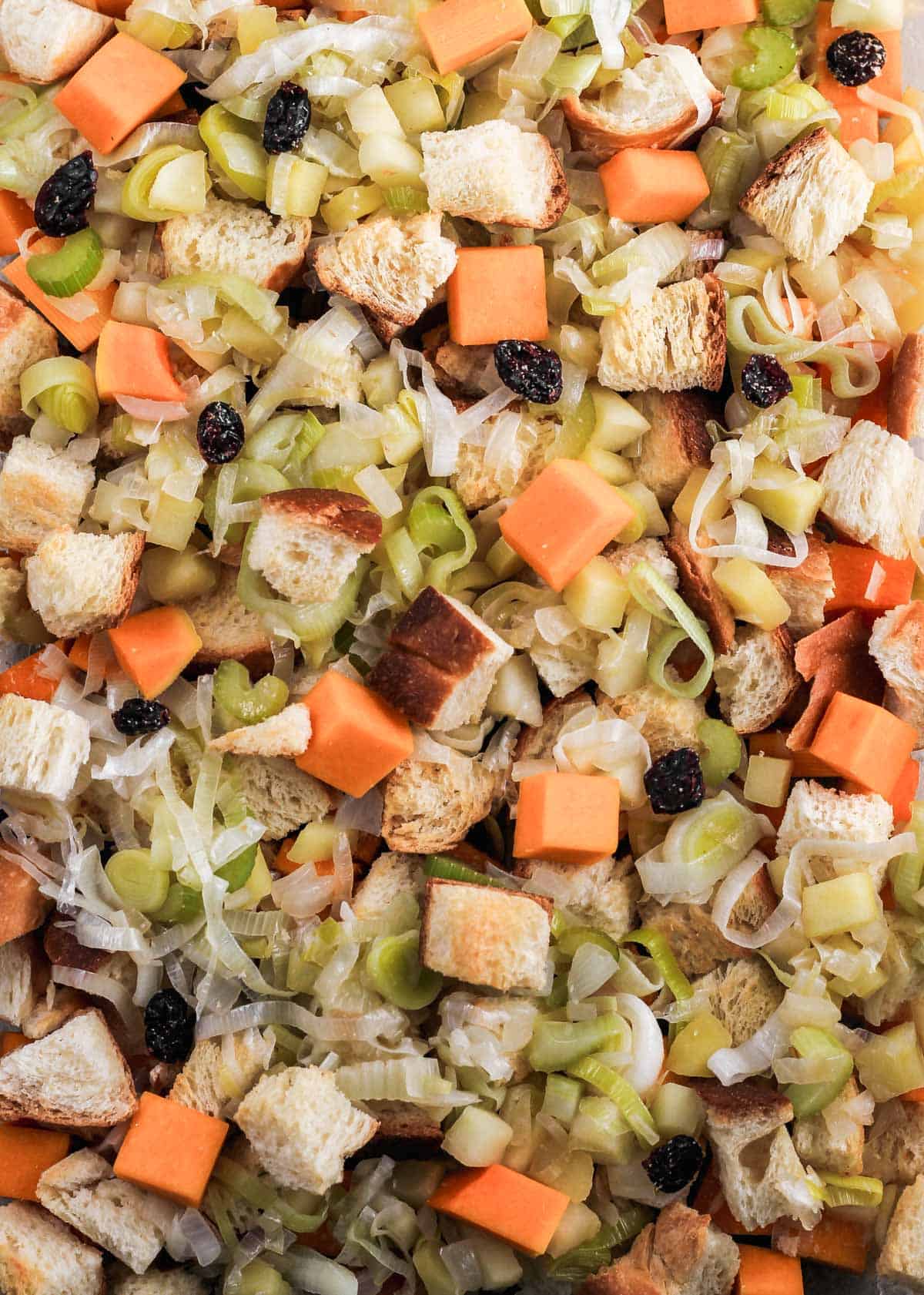 Layered challah, cooked vegetables, dried cranberries, and butternut squash in a baking dish.