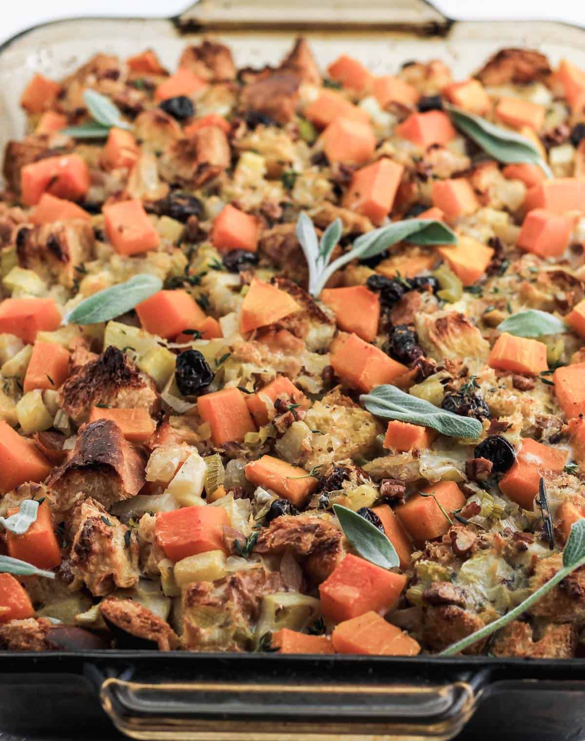 Butternut squash stuffing in a glass baking dish with leaves of sage on top.