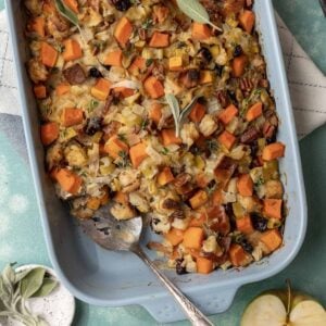 Baked butternut squash and apple stuffing in a blue baking dish with a serving spatula.