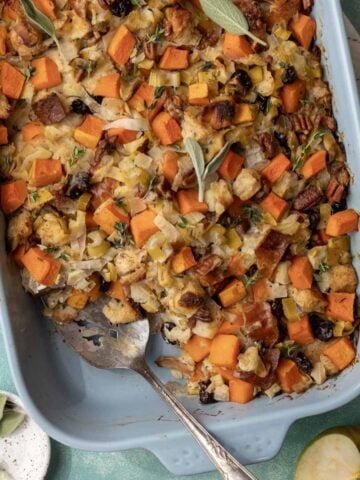 Baked butternut squash and apple stuffing in a blue baking dish with a serving spatula.