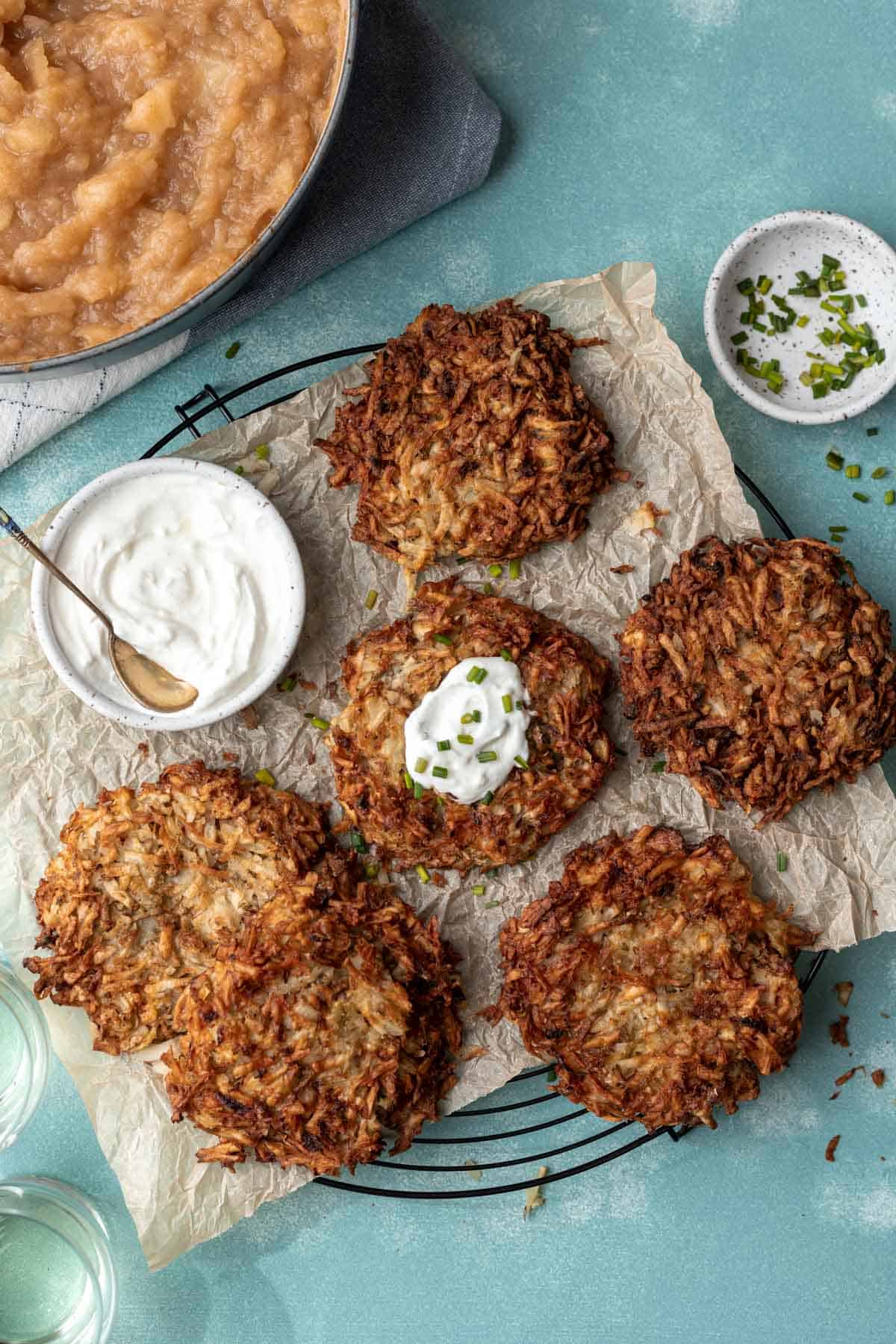 Potato latkes on a wire rack with a side of sour cream, applesauce, and chives.