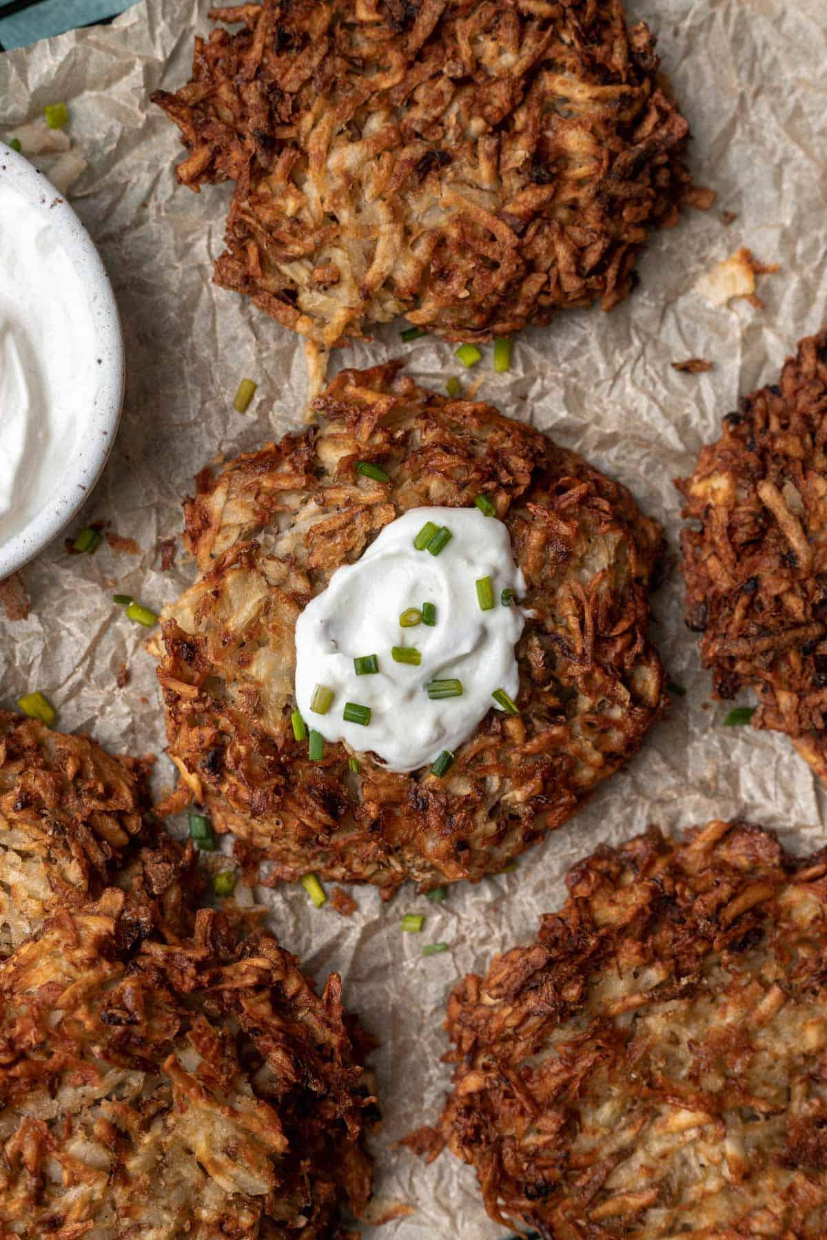 Air fryer potato latke in the middle of 4 others with a dollop of sour cream and a sprinkle of chives.