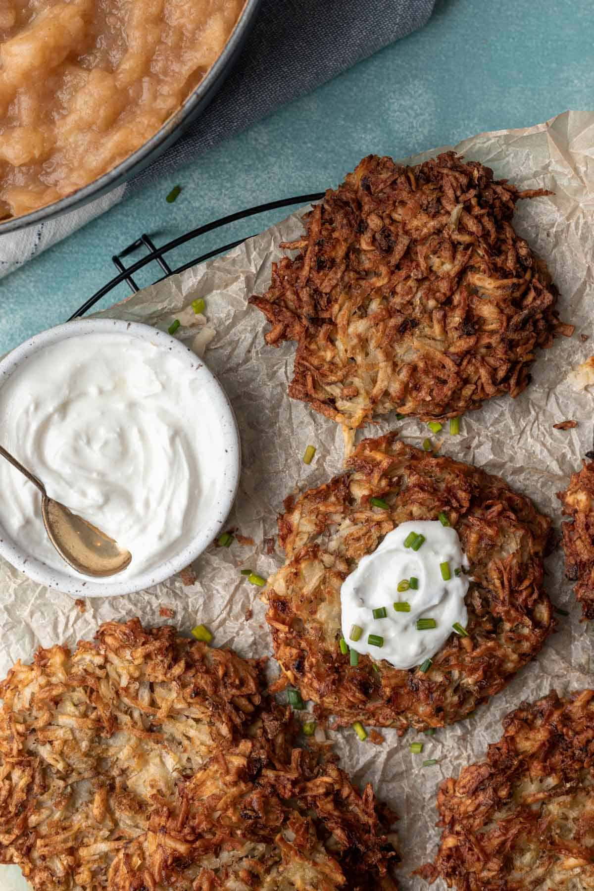 Air fryer potato latkes on a wire cooling rack with a side of sour cream and applesauce.