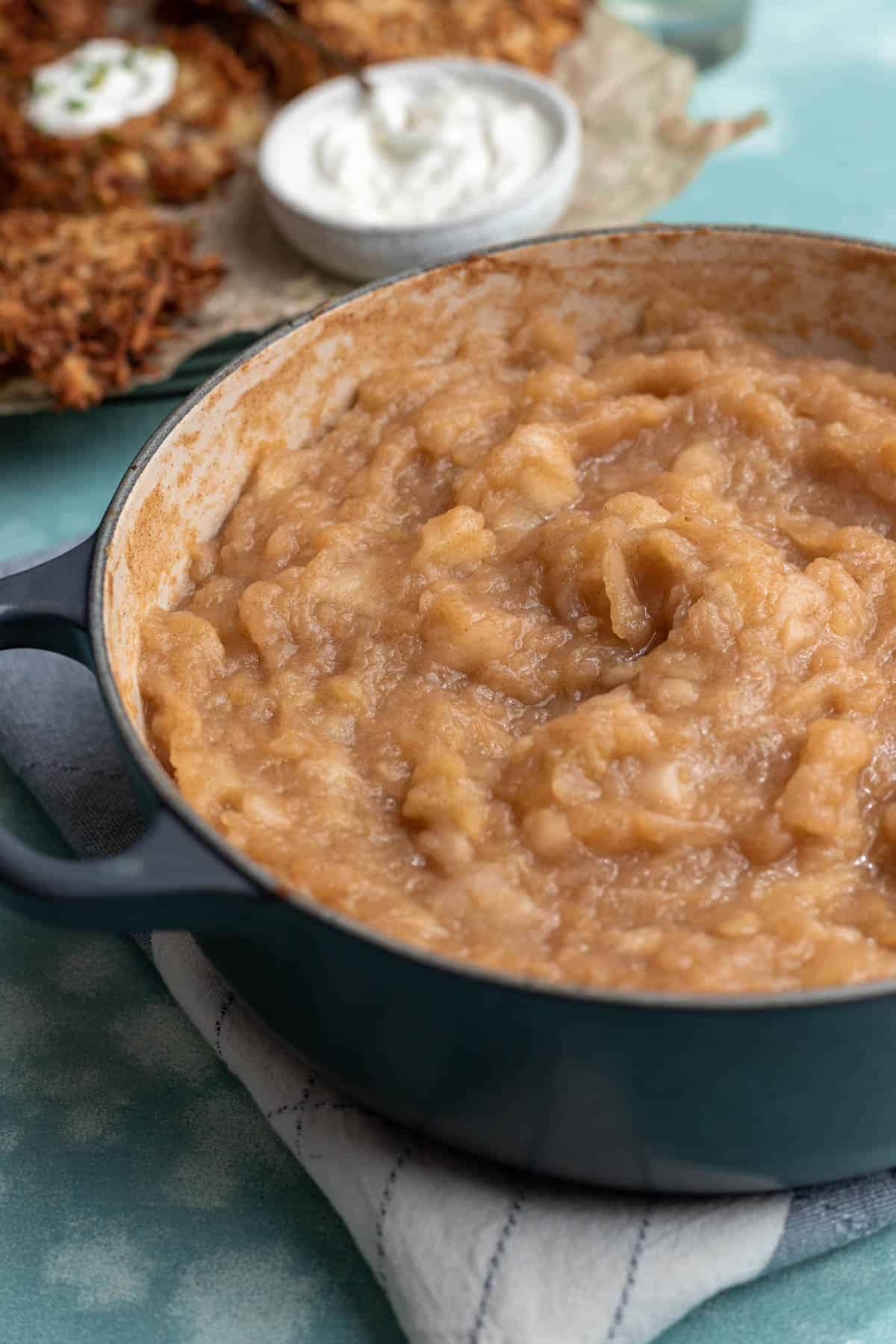 Cooked applesauce in a large stock pot with air fryer latkes behind it..