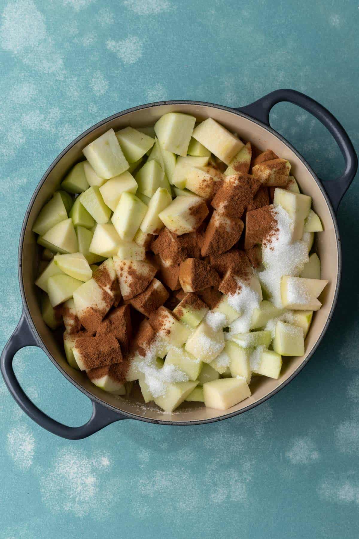 Chopped apples in a large stock pot with sugar and cinnamon on top.