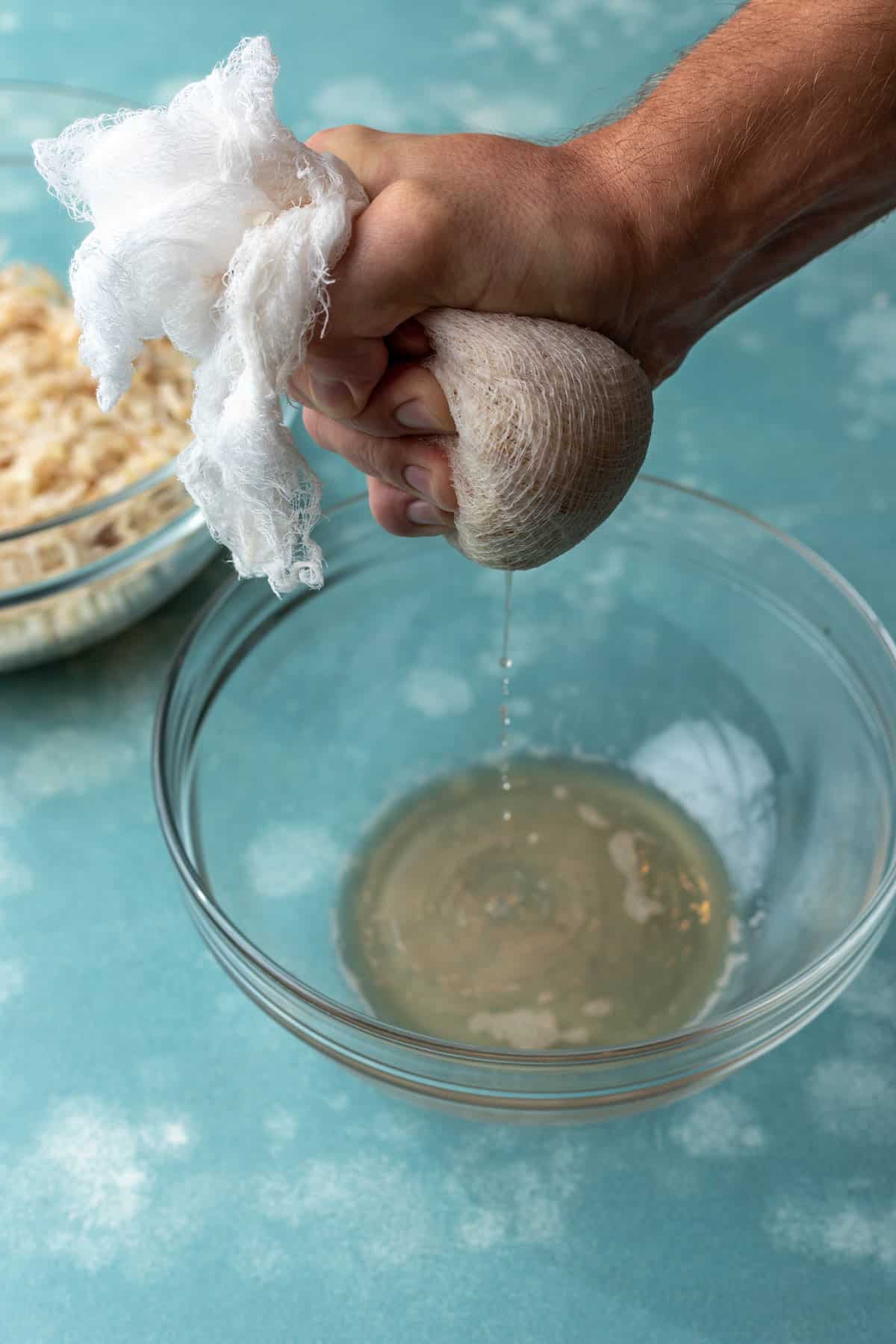 Shredded potatoes and onions in a cheesecloth with a hand squeezing extra water out.