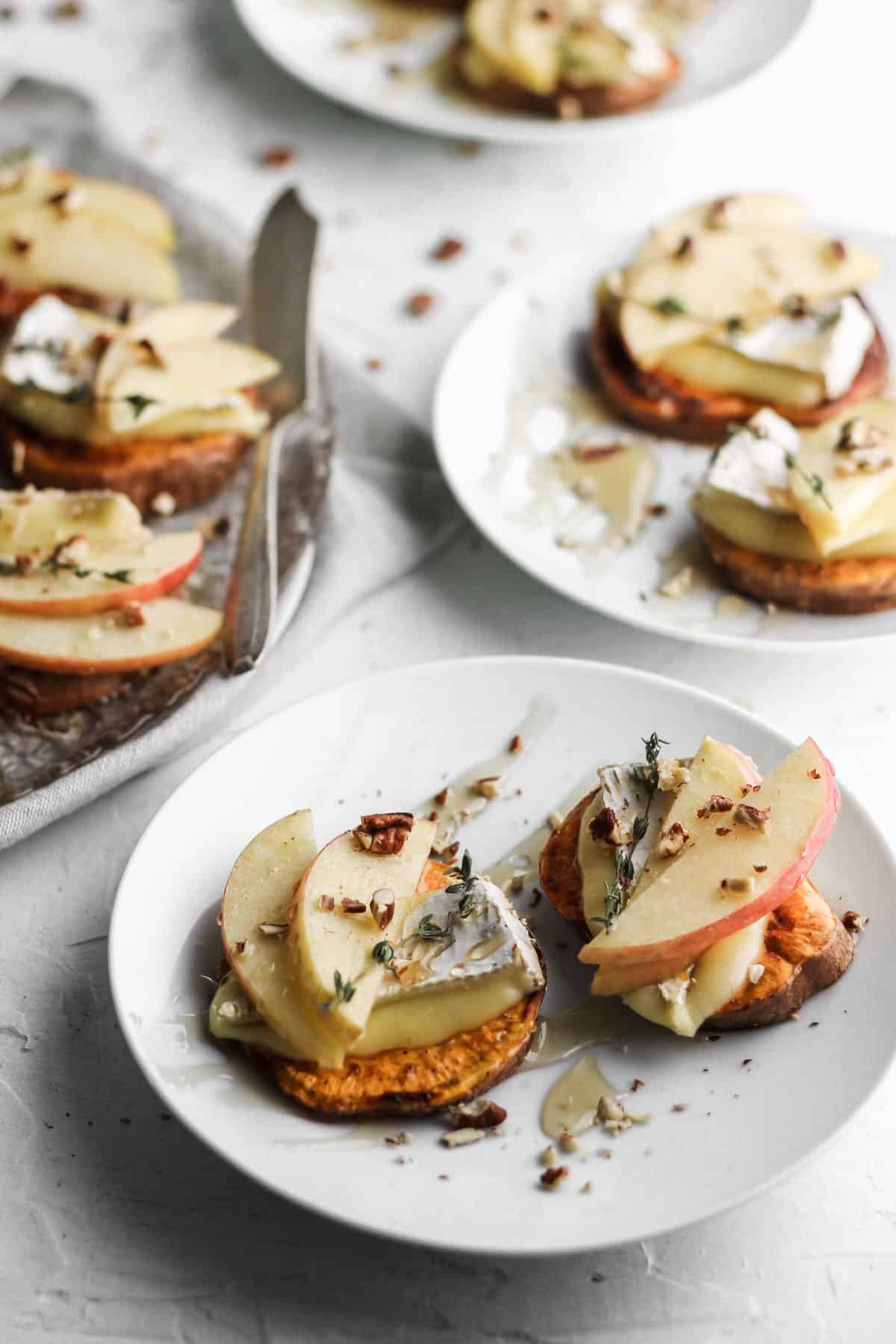 2 apple and brie sweet potato crostini on small white appetizer plates.