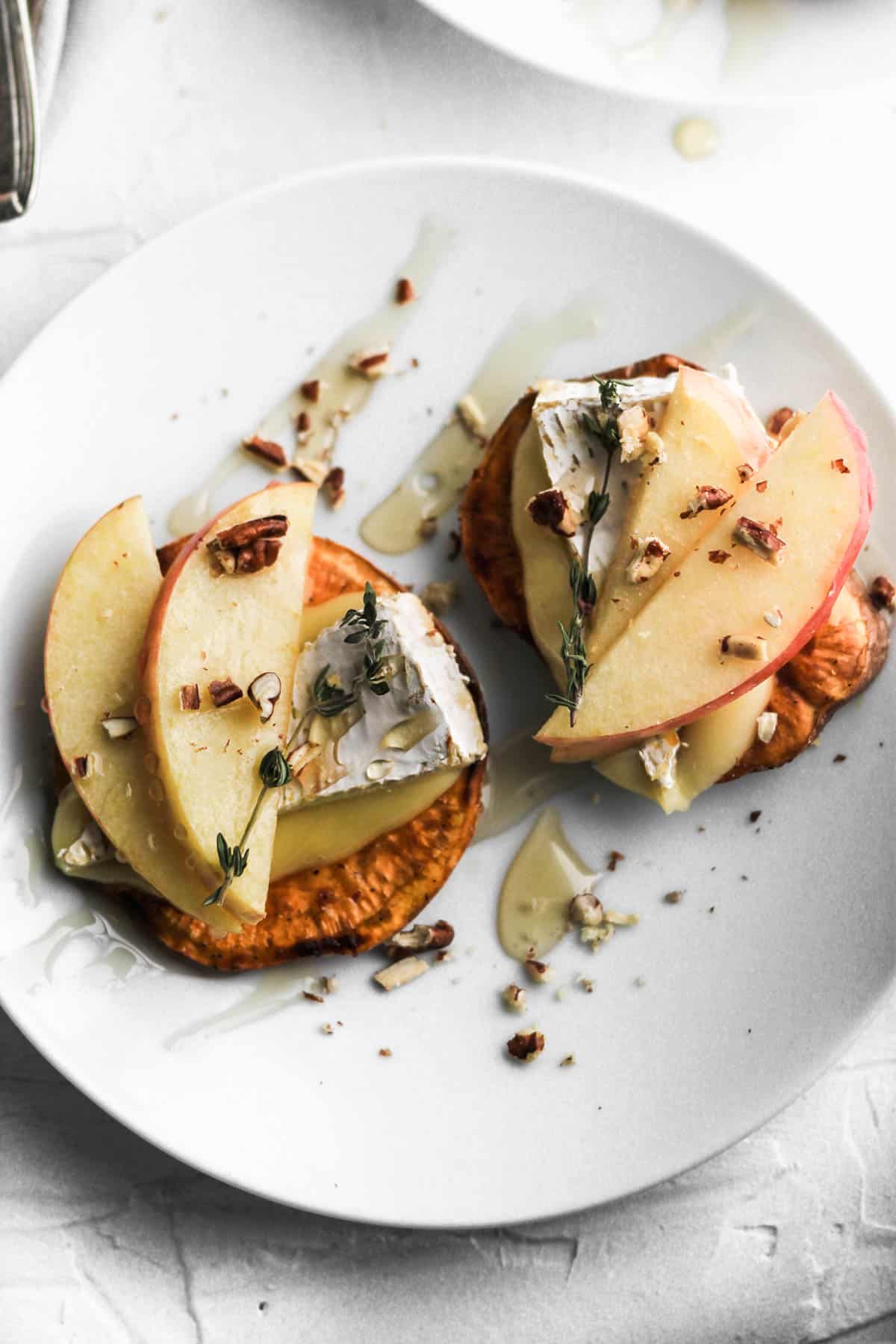 Overhead view of 2 apple and brie sweet potato crostini on a white appetizer plate.