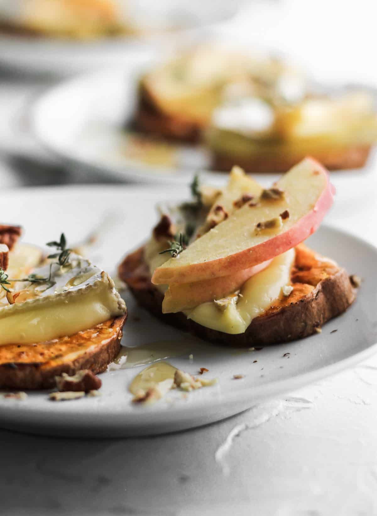 Side view of 2 apple and brie sweet potato bites on a white appetizer plate.