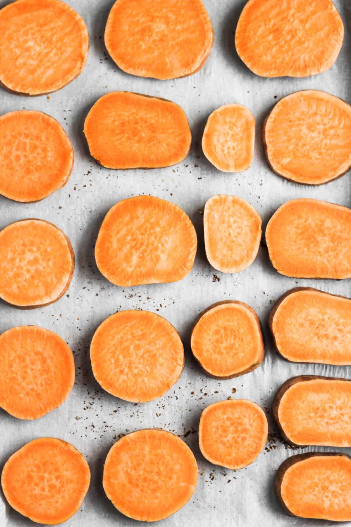 Sliced sweet potato circles on a parchment-lined sheet pan.